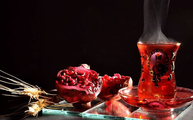 یک فنجان چای در کنار یک نصفه انار
