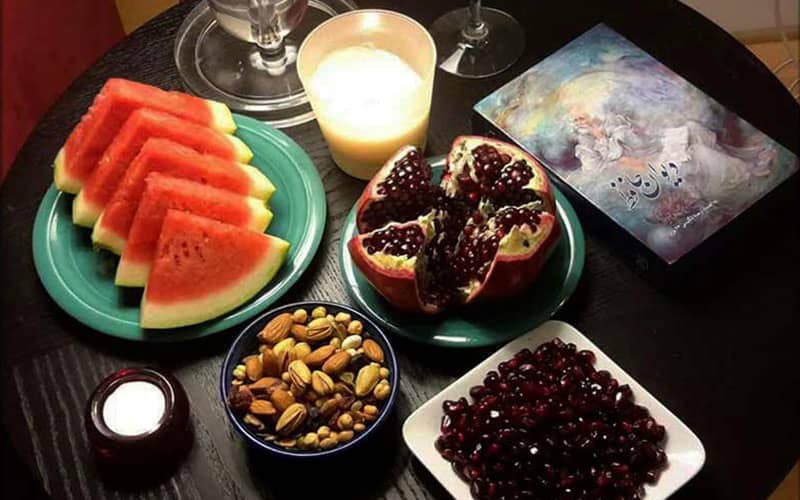هندوانه و انار دون شده و آجیل و شمعی روشن روی میز